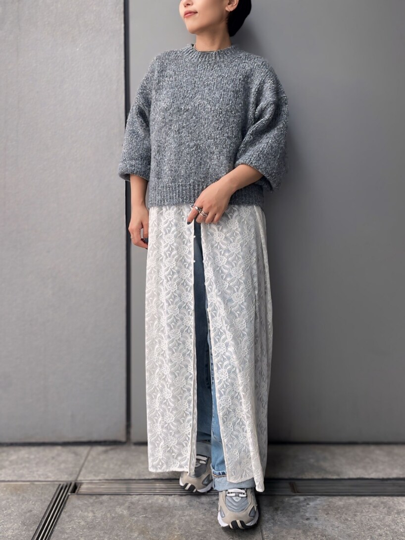 グレー系のニット/セーター、ホワイト系のワンピース、ブルー系のデニムパンツを着用したレディースの秋コーディネートの2枚目の写真