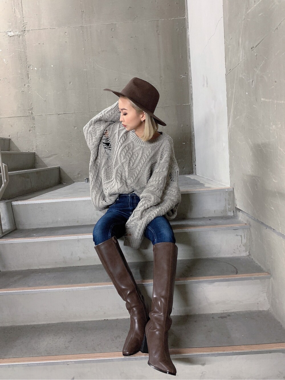 ブラウン系のブーツ、グレー系のニット/セーター、ブルー系のデニムパンツを着用したレディースの秋コーディネートの2枚目の写真