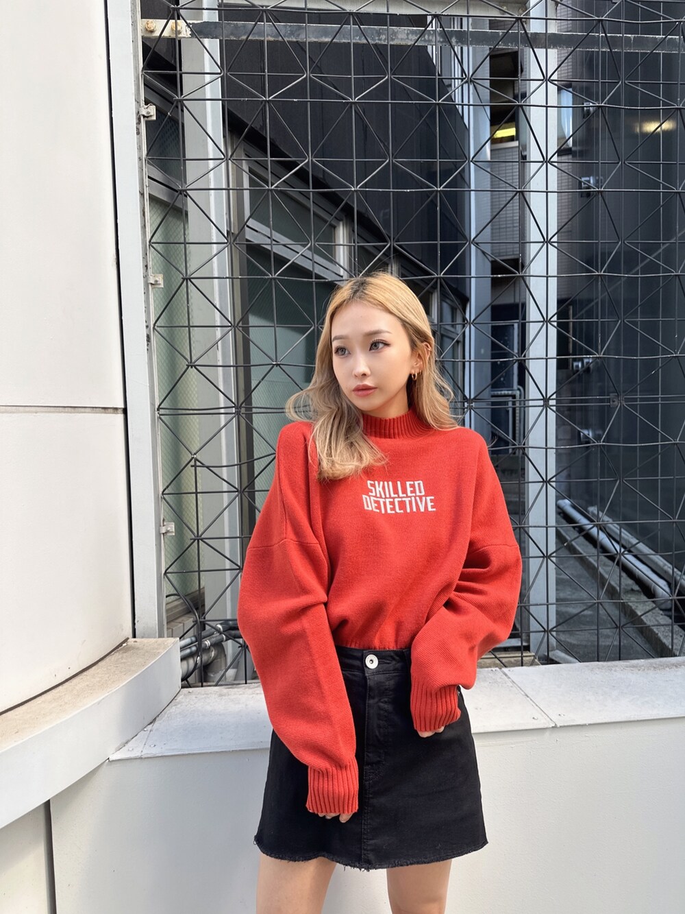 オレンジ系のニット/セーター、ブラック系のスカート、ブラック系のブーツを着用したレディースの秋コーディネートの3枚目の写真