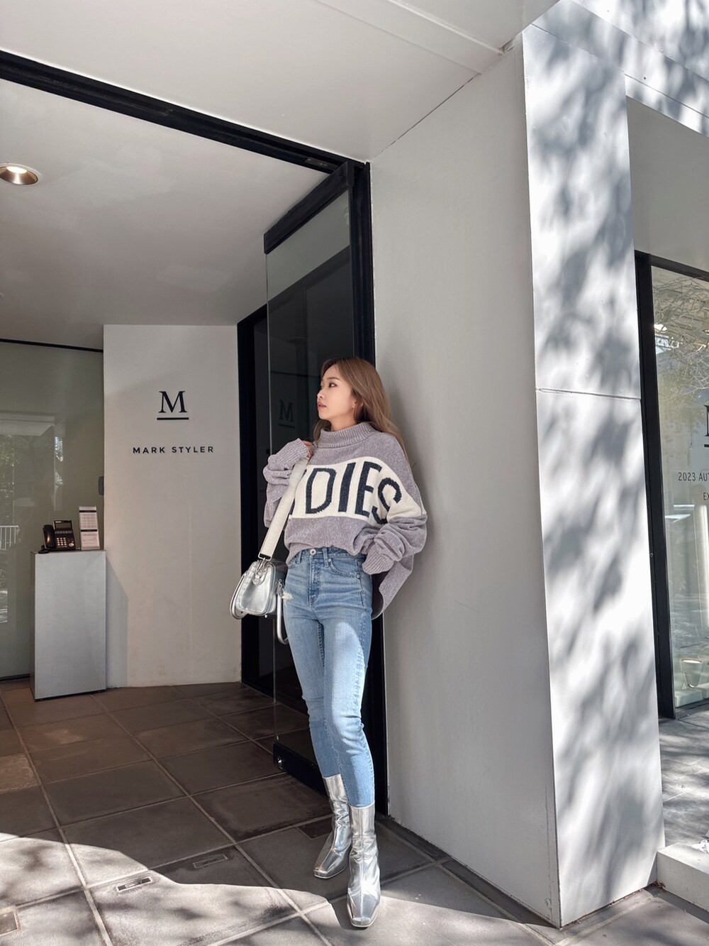 グレー系のニット/セーター、ブルー系のデニムパンツ、シルバー系のブーツを着用したレディースの秋コーディネートの2枚目の写真