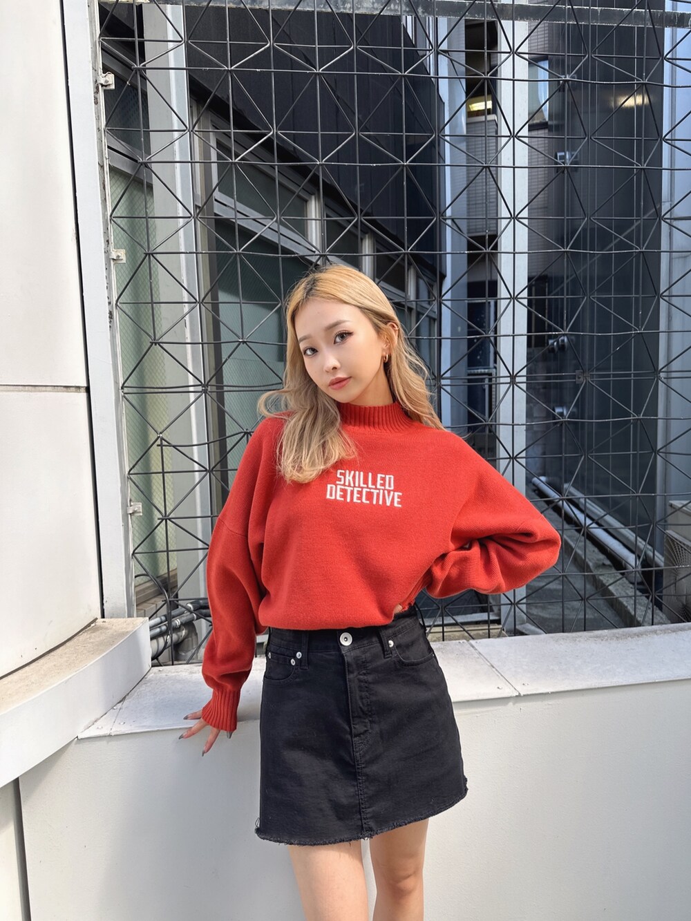 オレンジ系のニット/セーター、ブラック系のスカート、ブラック系のブーツを着用したレディースの秋コーディネートの4枚目の写真