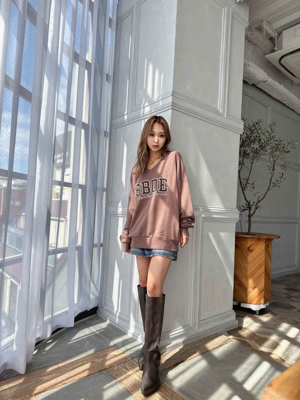 ベージュ系のスウェット、ブルー系のデニムスカート、ブラウン系のブーツを着用したレディースの秋コーディネートの2枚目の写真