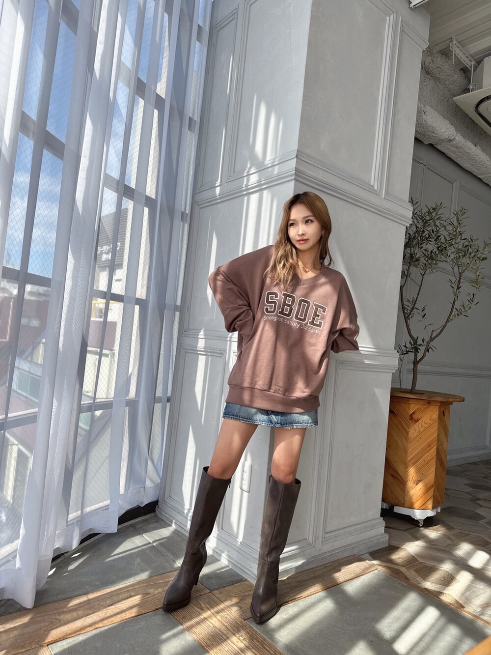 ベージュ系のスウェット、ブルー系のデニムスカート、ブラウン系のブーツを着用したレディースの秋コーディネートの3枚目の写真