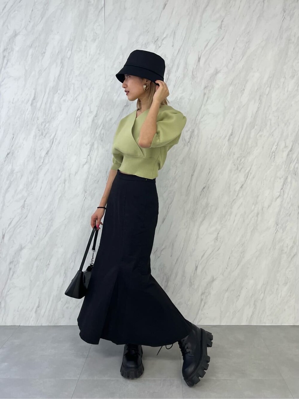 ブラック系のブーツ、ブラック系のスカート、イエロー系のニット/セーターを着用したレディースの春コーディネートの2枚目の写真