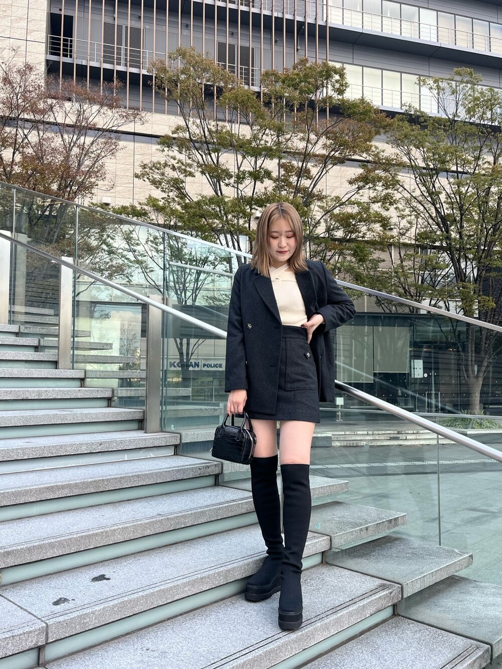 グレー系のテーラードジャケット、ホワイト系のニット/セーター、グレー系のスカートを着用したレディースの秋コーディネートの2枚目の写真