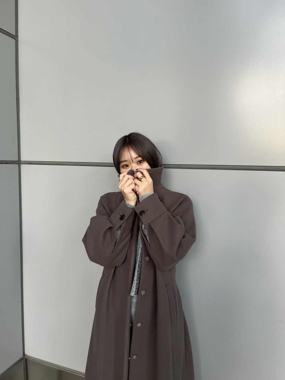 グレー系のニット/セーター、グレー系のスカート、ブラウン系のステンカラーコートを着用したレディースの冬コーディネートの2枚目の写真
