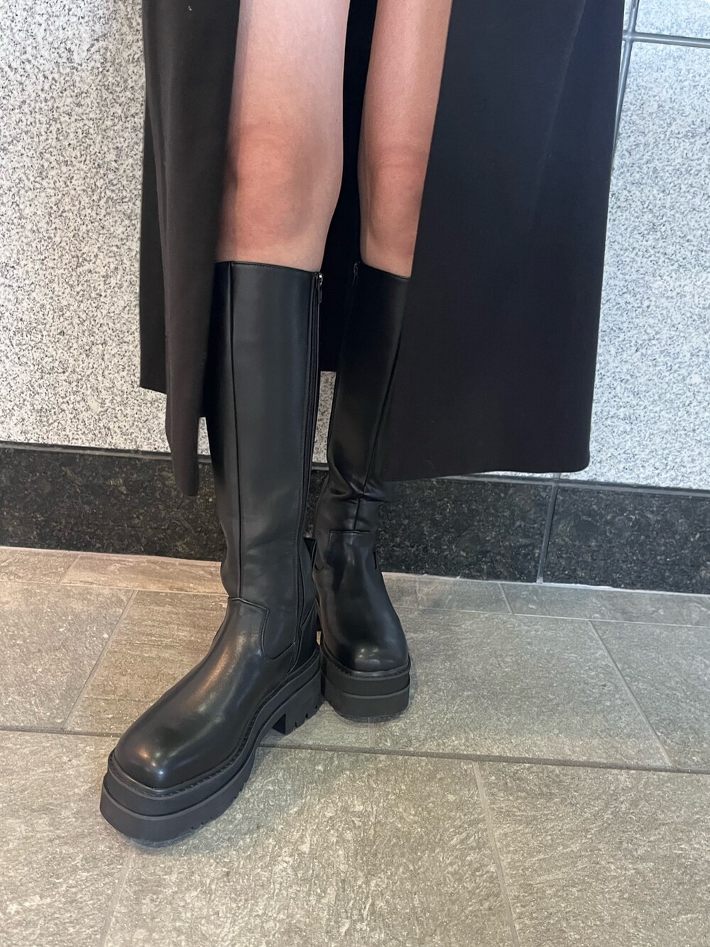 ブラック系のステンカラーコート、グレー系のその他パンツ、ブラック系のブーツを着用したレディースの冬コーディネートの6枚目の写真