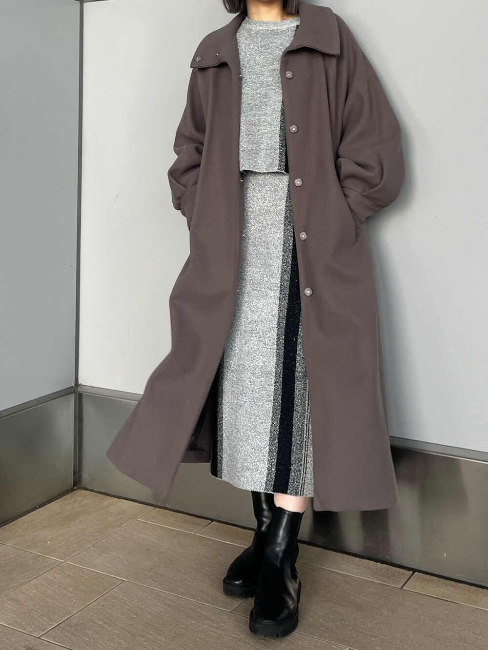 グレー系のニット/セーター、グレー系のスカート、ブラウン系のステンカラーコートを着用したレディースの冬コーディネートの7枚目の写真