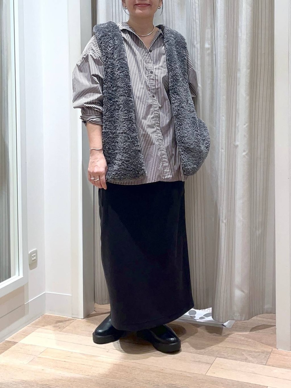 グレー系のベスト、ブラック系のスカート、ブラック系のブーツを着用したレディースの秋コーディネートの4枚目の写真