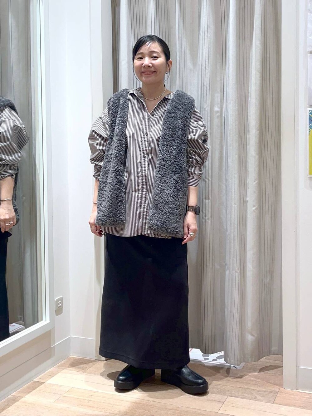 グレー系のベスト、ブラック系のスカート、ブラック系のブーツを着用したレディースの秋コーディネートの5枚目の写真