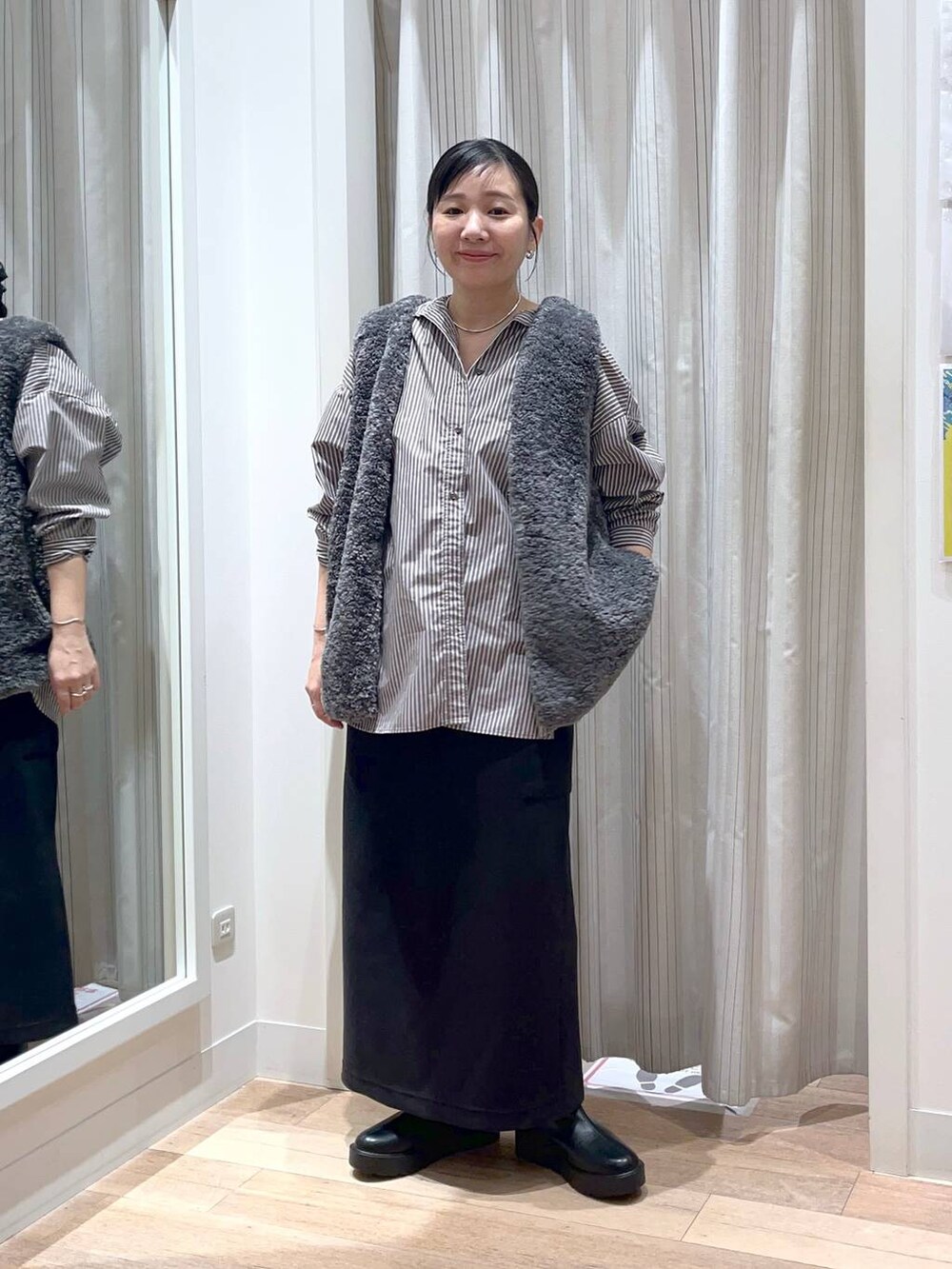 グレー系のベスト、ブラック系のスカート、ブラック系のブーツを着用したレディースの秋コーディネートの7枚目の写真