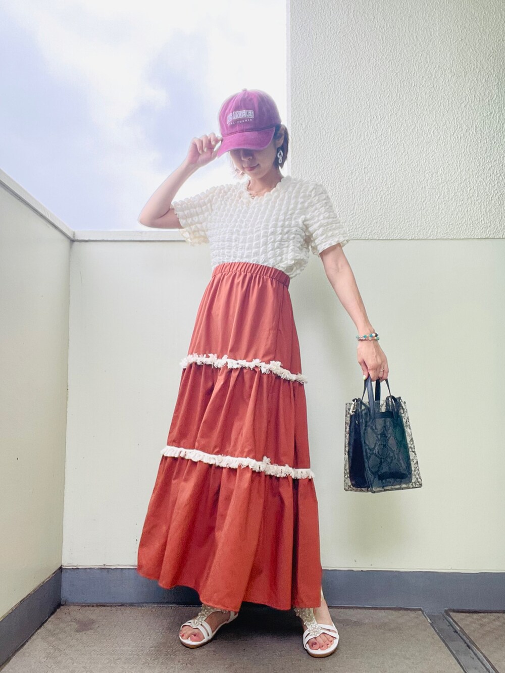 ホワイト系のサンダル、ブラウン系のスカート、ブラック系のバッグを着用したレディースの夏コーディネートの2枚目の写真