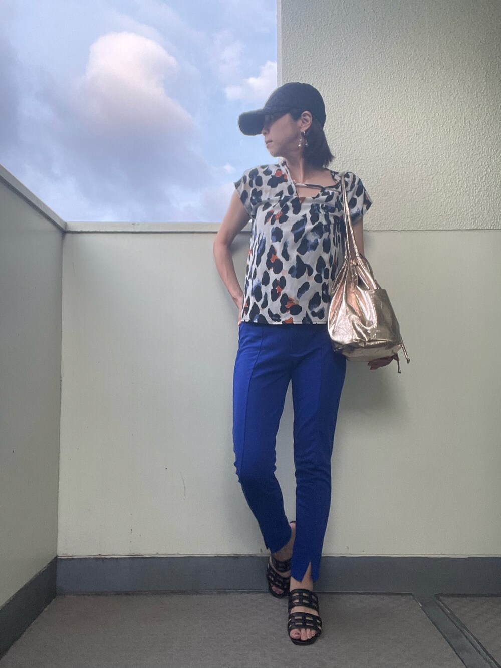 ブルー系のパンツ、ゴールド系のトートバッグ、ブラック系のサンダルを着用したレディースの夏コーディネートの2枚目の写真