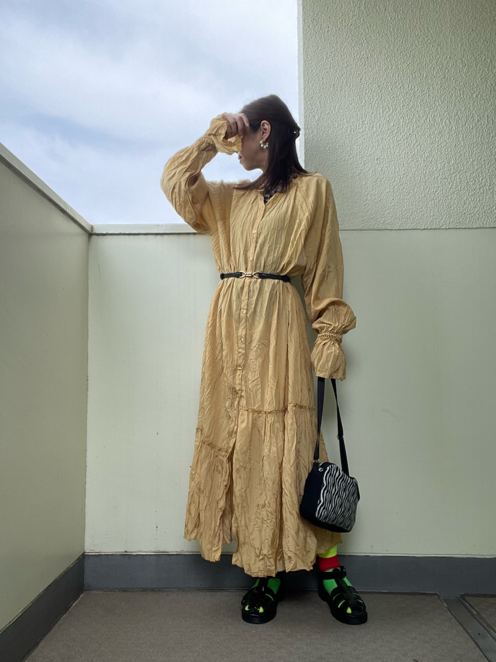 イエロー系のワンピース、ブラック系のサンダル、ホワイト系のショルダーバッグを着用したレディースの春コーディネートの2枚目の写真