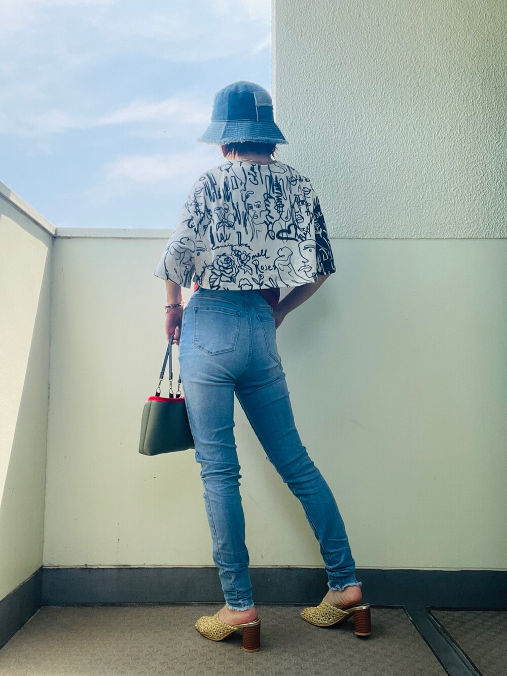 グリーン系のバッグ、ブルー系のデニムパンツ、ゴールド系のサンダルを着用したレディースの夏コーディネートの2枚目の写真