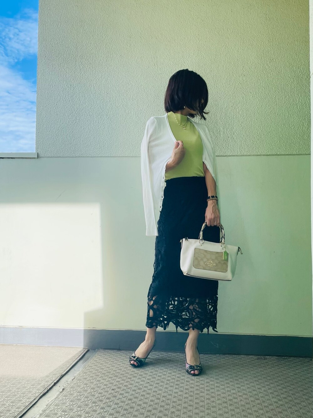 グリーン系のニット/セーター、ブラック系のスカート、ホワイト系のカーディガン/ボレロを着用したレディースの夏コーディネートの2枚目の写真