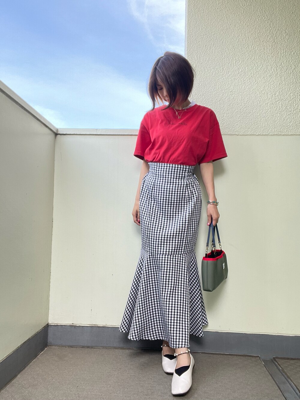 ブラック系のスカート、グリーン系のバッグ、ホワイト系のシューズを着用したレディースの夏コーディネートの2枚目の写真