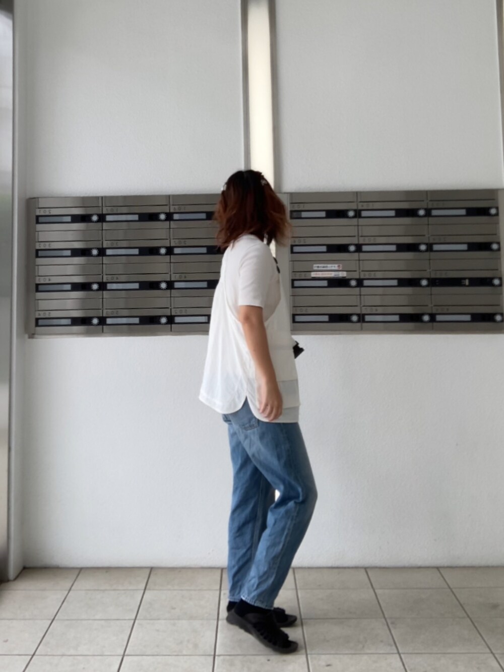 ブラック系のサンダル、ホワイト系のベスト、ブルー系のデニムパンツを着用したレディースの夏コーディネートの2枚目の写真