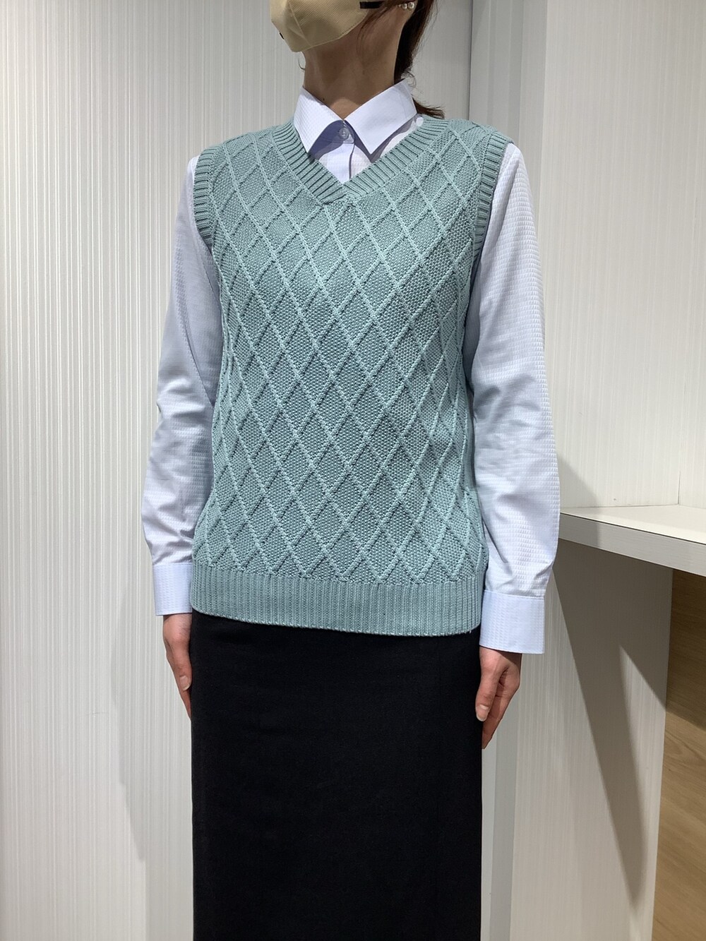 ブルー系のビジネスシャツ、グリーン系のベストを着用したレディースの冬コーディネートの2枚目の写真