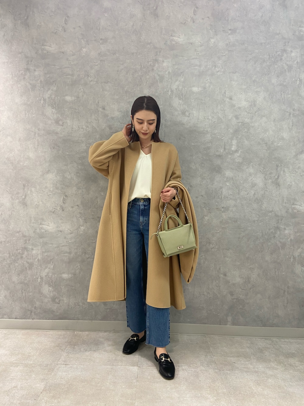 グリーン系のハンドバッグ、ホワイト系のシャツ/ブラウス、ベージュ系のノーカラーコートを着用したレディースの冬コーディネートの2枚目の写真