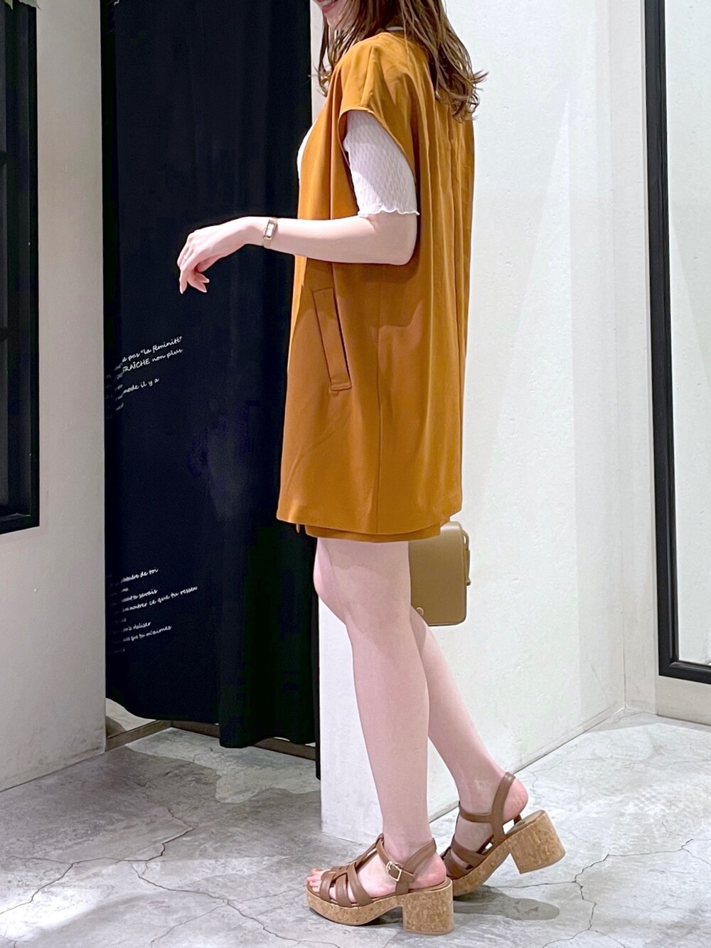 オレンジ系のベスト、ホワイト系のTシャツ/カットソー、ベージュ系のショルダーバッグを着用したレディースの夏コーディネートの4枚目の写真