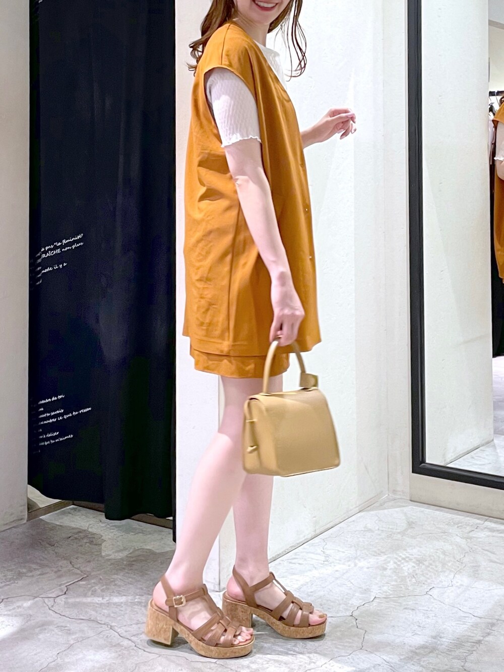 オレンジ系のベスト、ホワイト系のTシャツ/カットソー、ベージュ系のショルダーバッグを着用したレディースの夏コーディネートの2枚目の写真