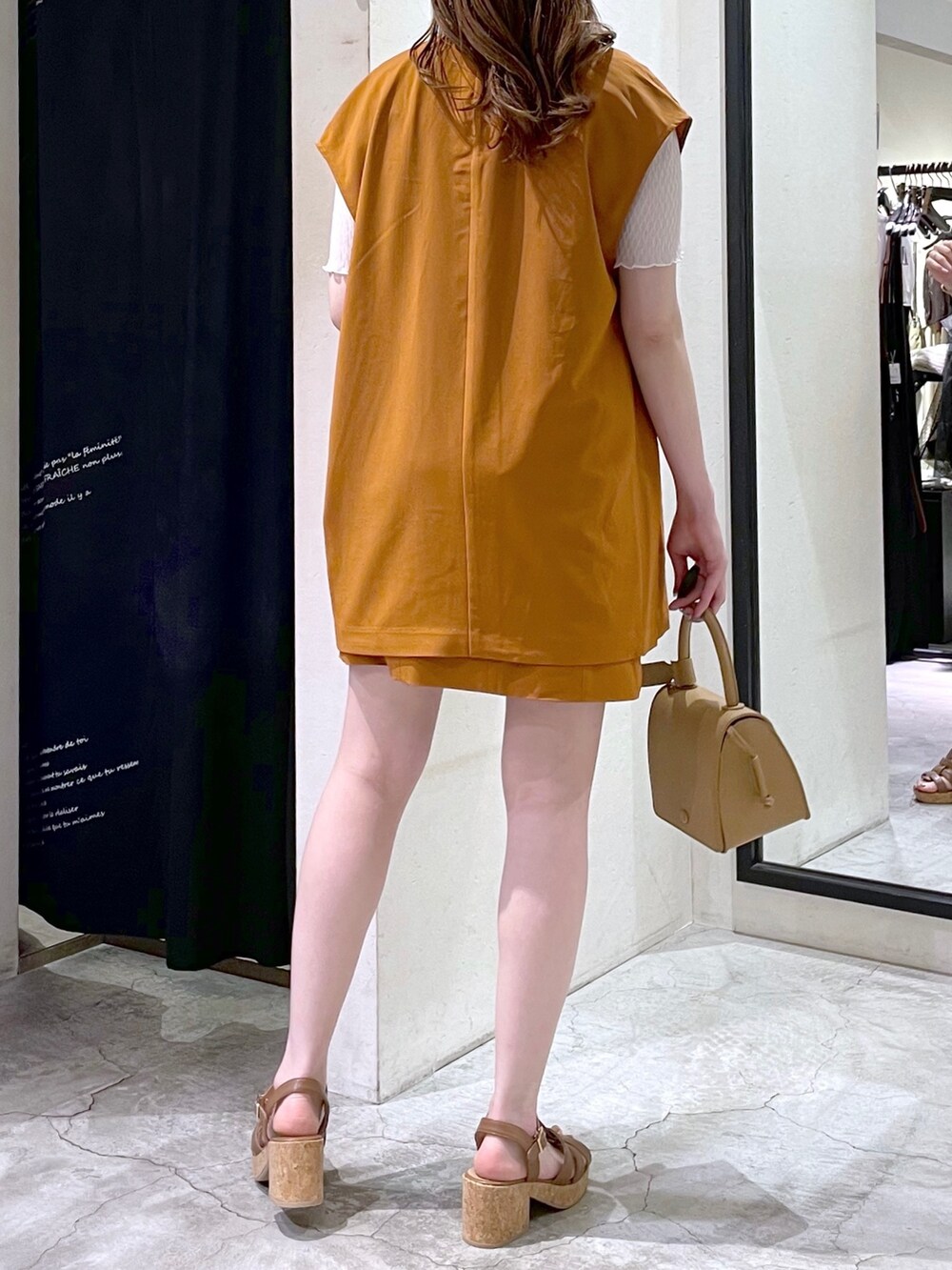 オレンジ系のベスト、ホワイト系のTシャツ/カットソー、ベージュ系のショルダーバッグを着用したレディースの夏コーディネートの3枚目の写真