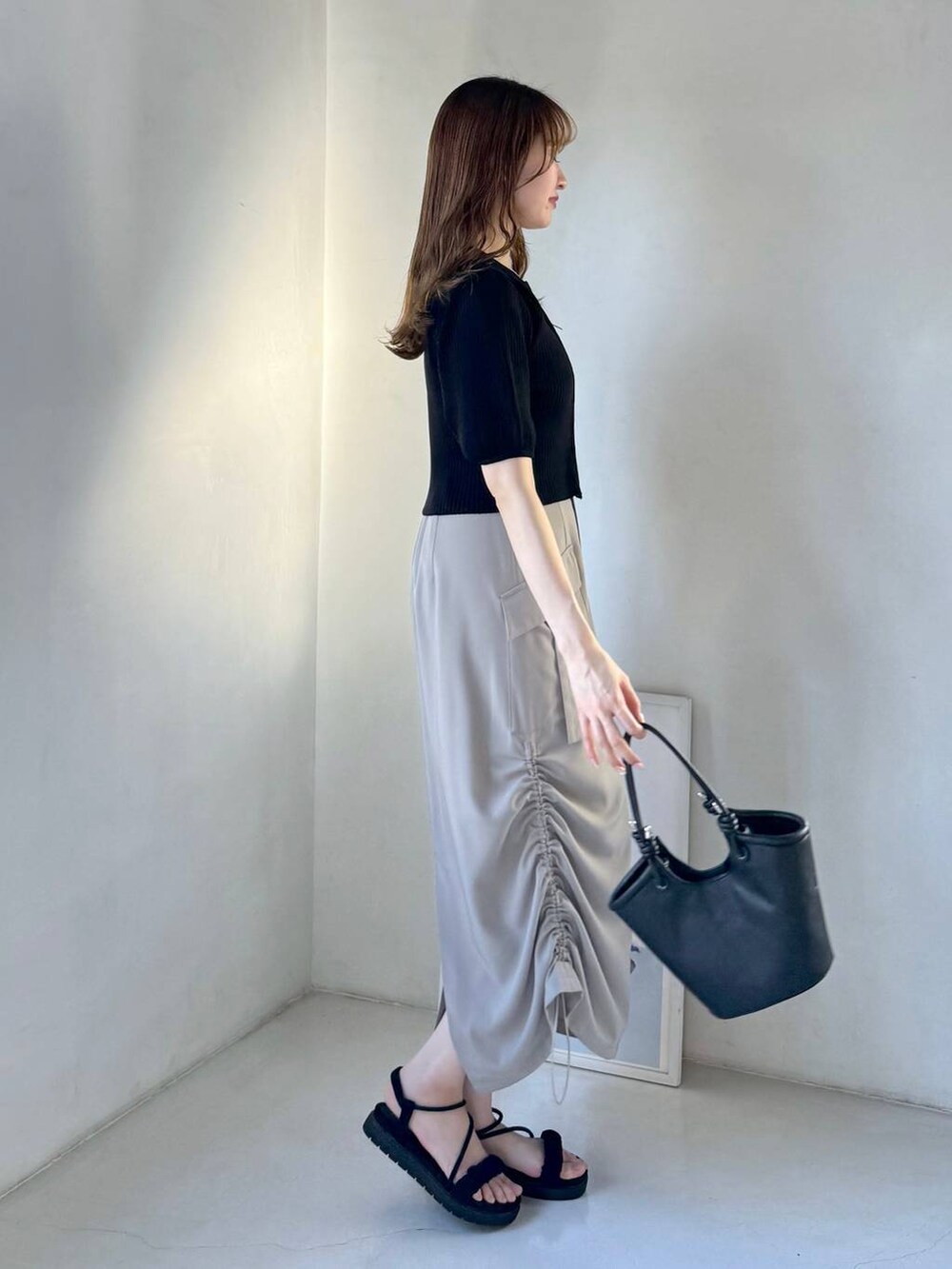 ベージュ系のスカート、ブラック系のサンダル、ブラック系のハンドバッグを着用したレディースの春コーディネートの2枚目の写真