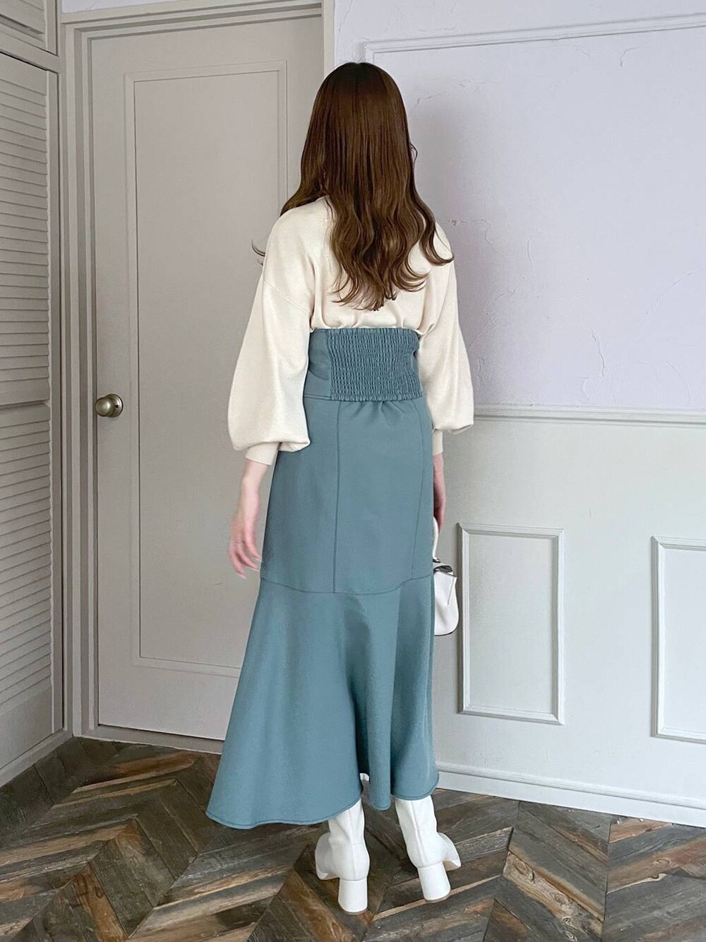 ホワイト系のハンドバッグ、ホワイト系のブーツ、ブルー系のスカートを着用したレディースの秋コーディネートの2枚目の写真