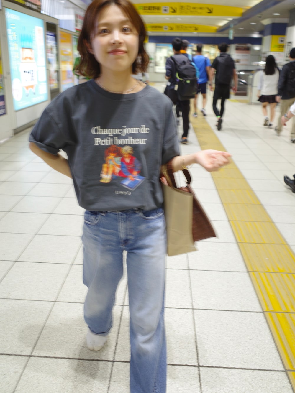 グレー系のTシャツ/カットソー、ブルー系のデニムパンツ、ブラウン系のハンドバッグを着用したレディースの夏コーディネートの2枚目の写真
