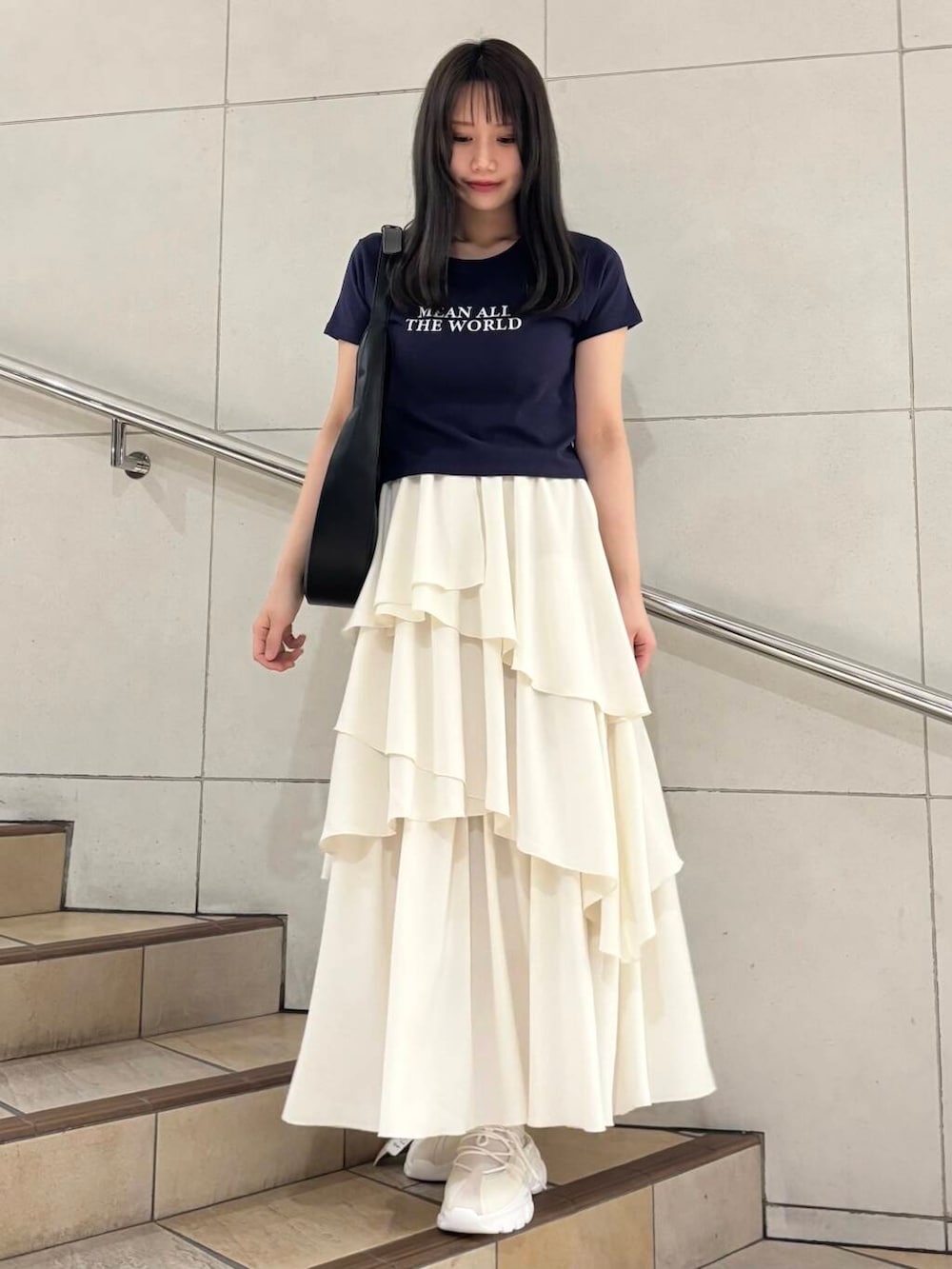 ブラック系のショルダーバッグ、ホワイト系のスカート、ホワイト系のスニーカーを着用したレディースの春コーディネートの2枚目の写真