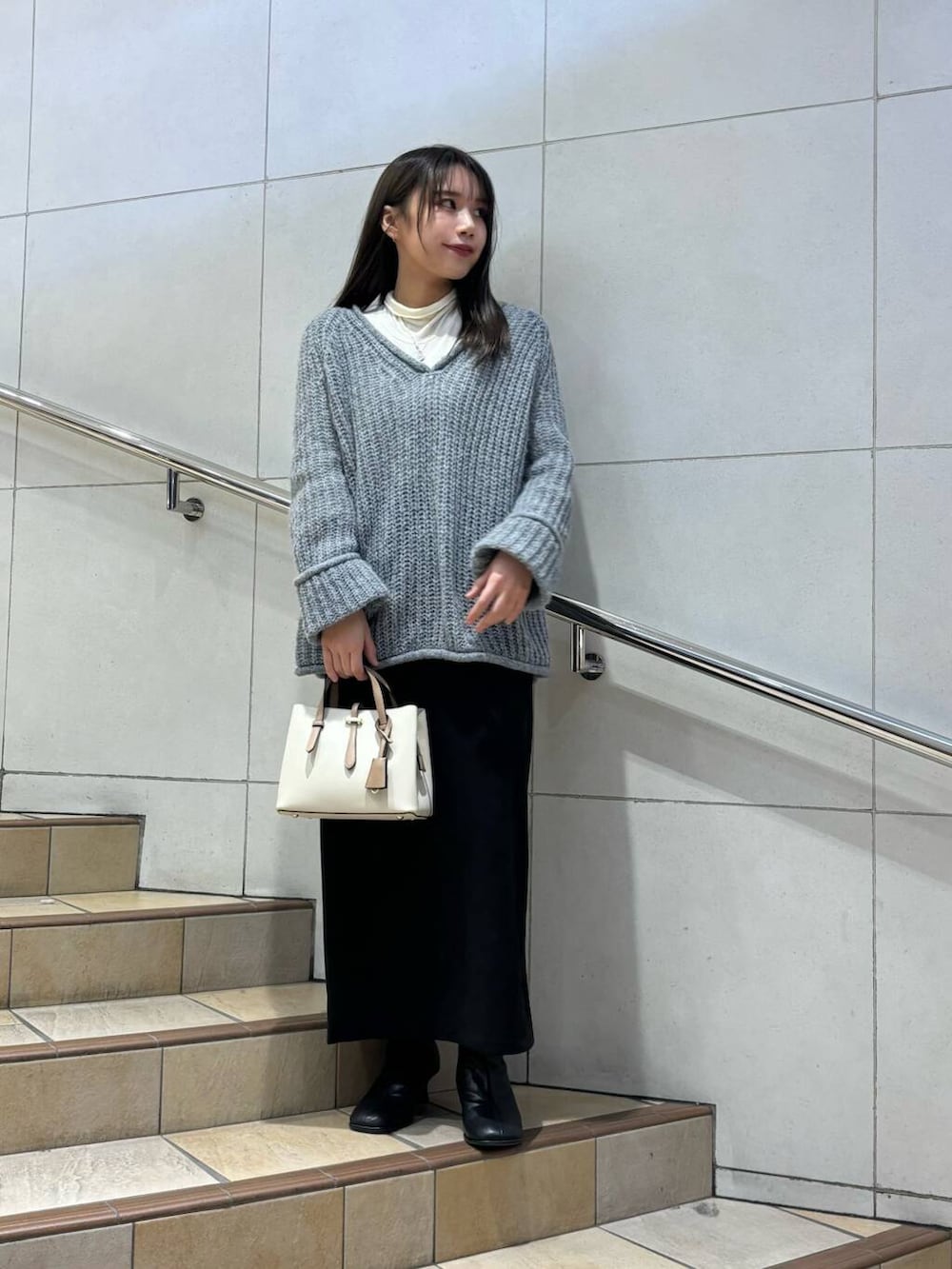 ホワイト系のハンドバッグ、ブラック系のブーツ、ホワイト系のTシャツ/カットソーを着用したレディースの冬コーディネートの2枚目の写真