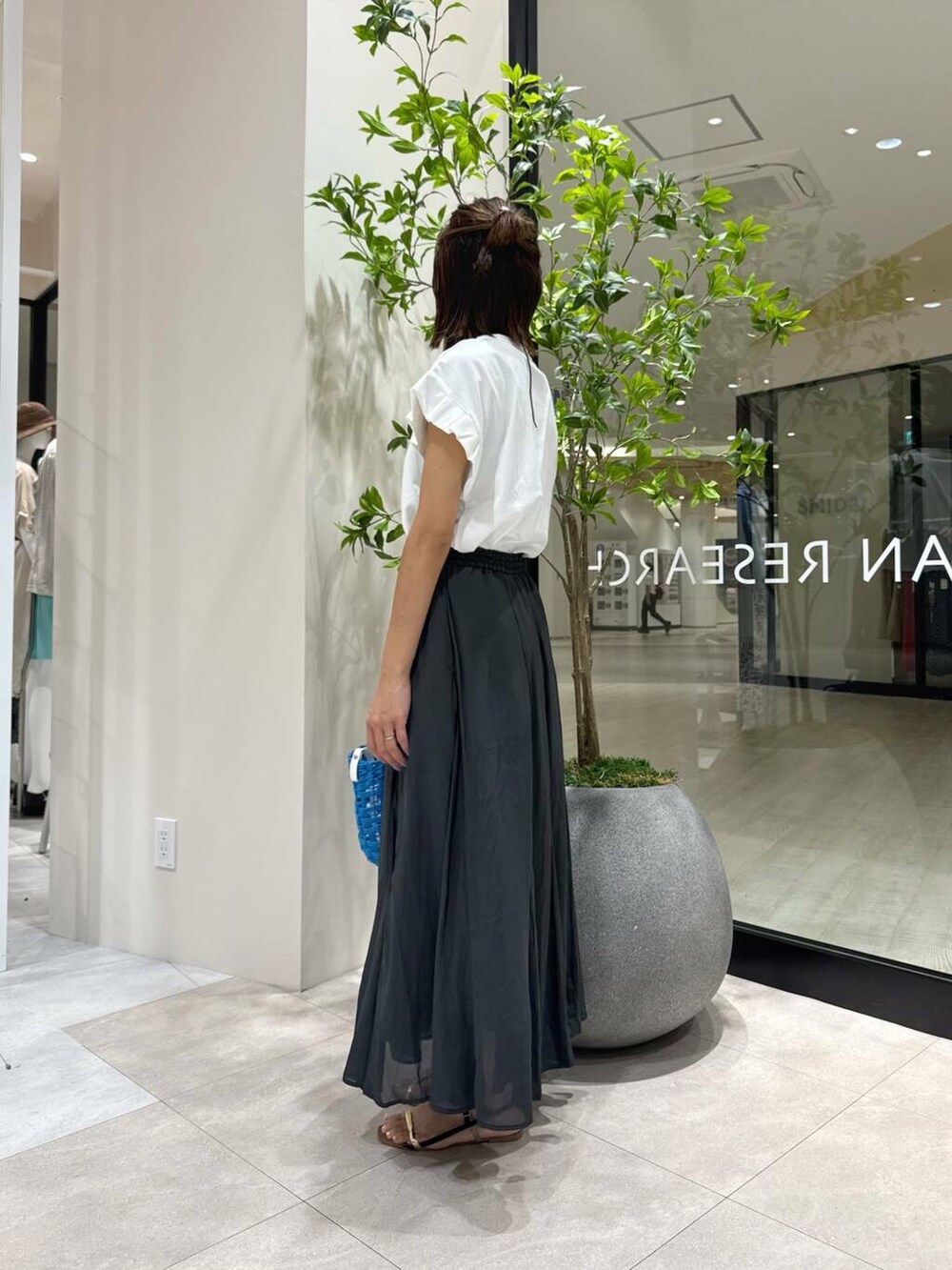 ブラック系のサンダル、ブルー系のかごバッグ、ブラック系のスカートを着用したレディースの夏コーディネートの2枚目の写真