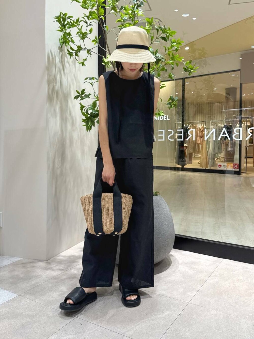 ベージュ系のトートバッグ、ブラック系のサンダル、ブラック系のセットアップを着用したレディースの夏コーディネートの5枚目の写真