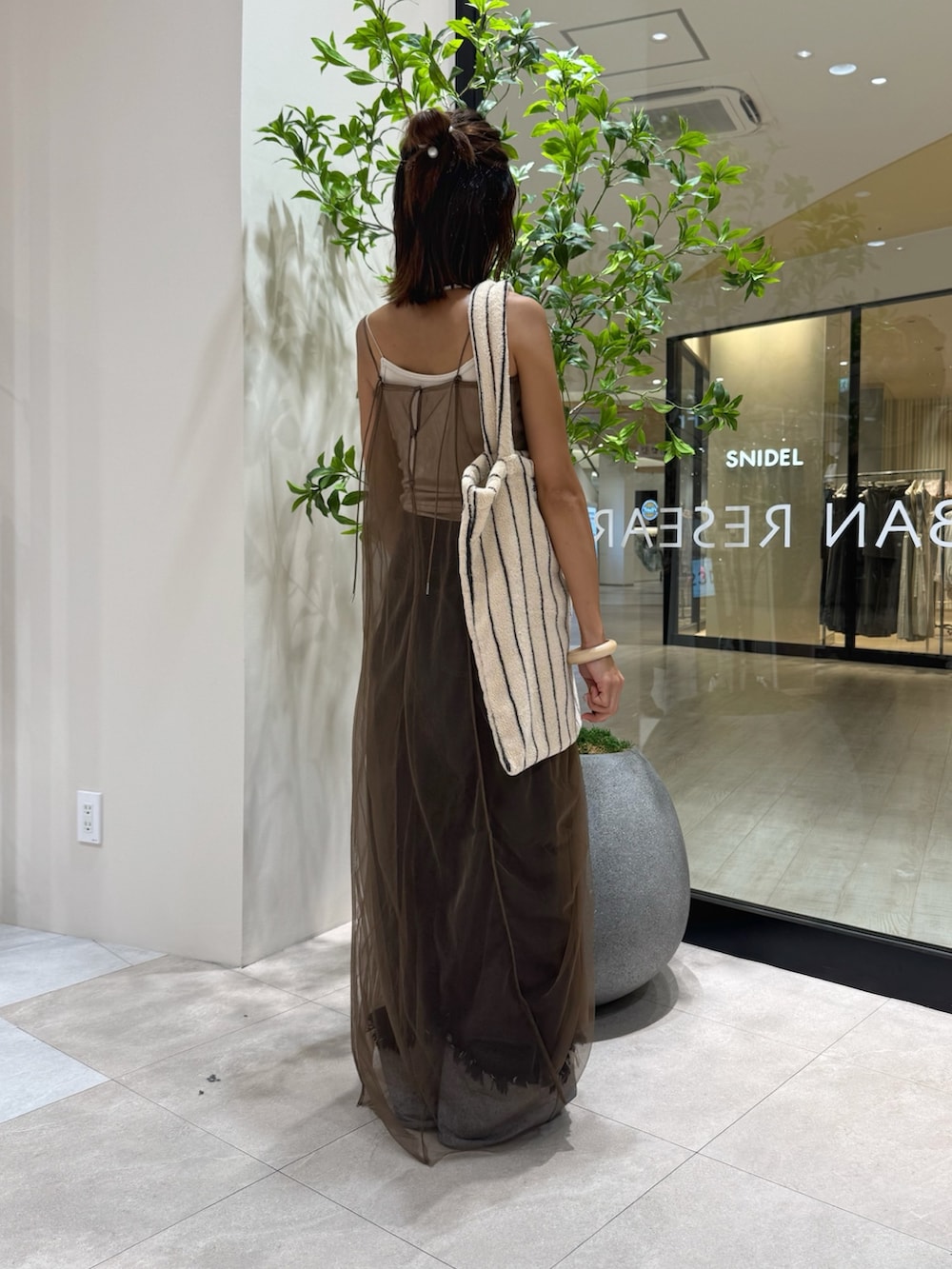 ベージュ系のキャミソール、ブラウン系のワンピース、ブルー系のデニムパンツを着用したレディースの秋コーディネートの2枚目の写真