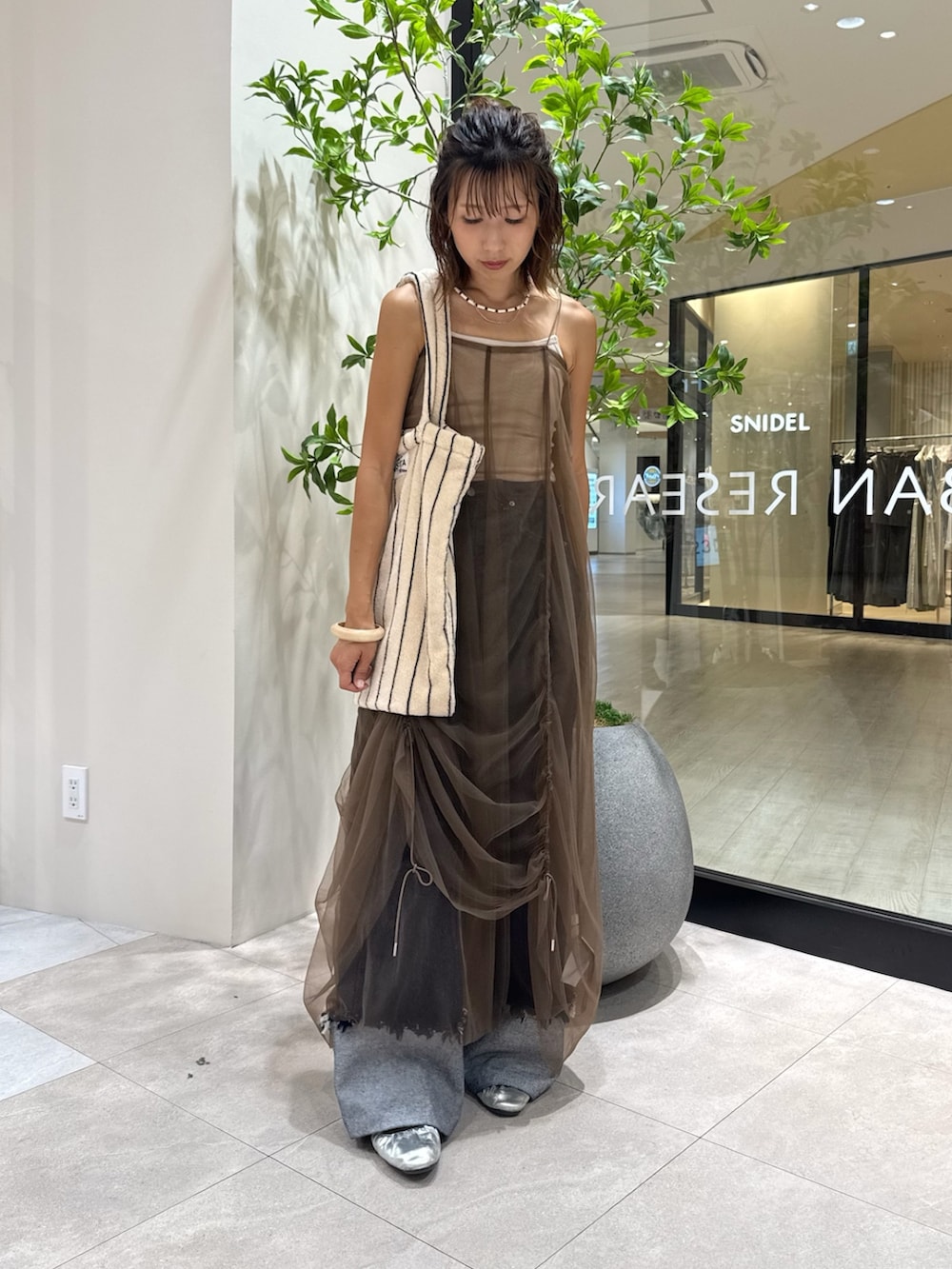 ベージュ系のキャミソール、ブラウン系のワンピース、ブルー系のデニムパンツを着用したレディースの秋コーディネートの5枚目の写真