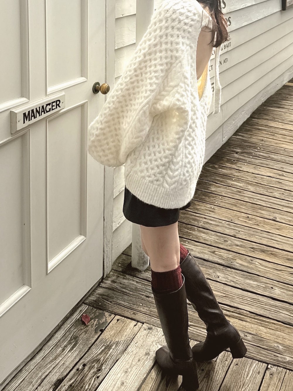 ブラウン系のブーツ、ホワイト系のニット/セーター、ホワイト系のキャミソールを着用したレディースの冬コーディネートの2枚目の写真