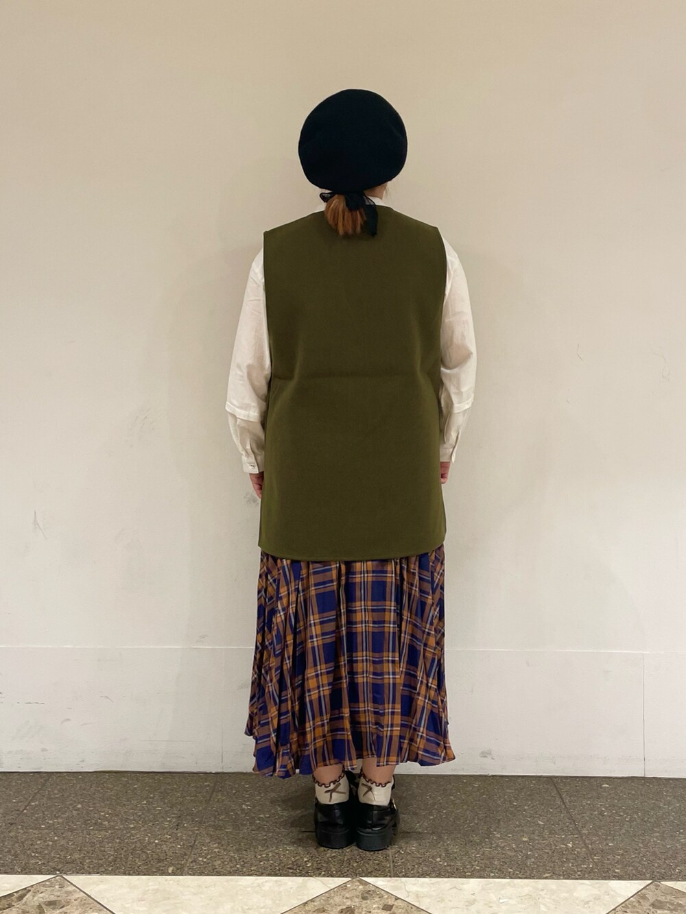 グリーン系のベスト、ホワイト系のチュニック、ブルー系のスカートを着用したレディースの秋コーディネートの3枚目の写真