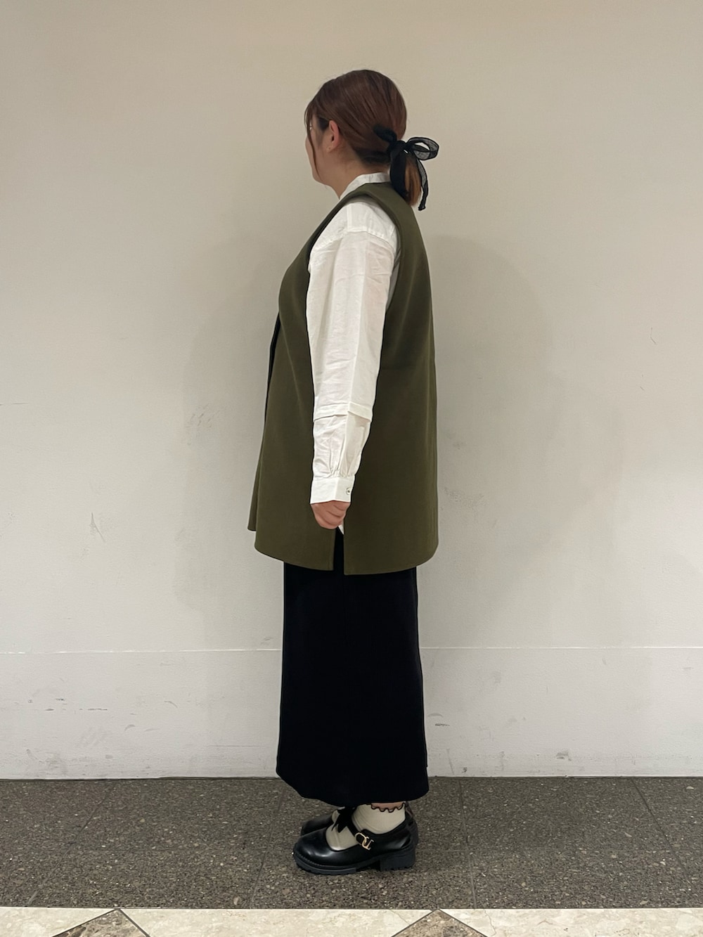 グリーン系のベスト、ホワイト系のチュニック、ブラック系のスカートを着用したレディースの秋コーディネートの2枚目の写真