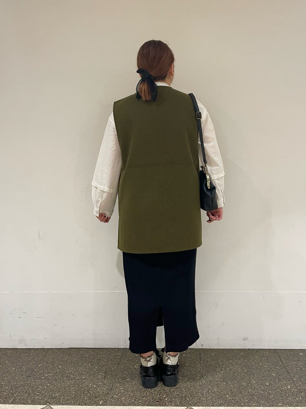 グリーン系のベスト、ホワイト系のチュニック、ブラック系のスカートを着用したレディースの秋コーディネートの3枚目の写真