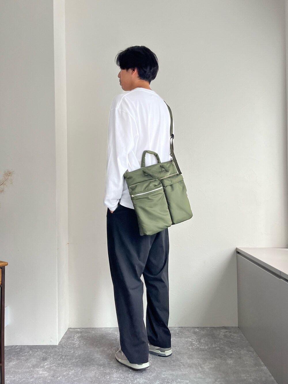 グリーン系のショルダーバッグ、ブラック系のスラックス、ホワイト系のTシャツ/カットソーを着用したメンズの夏コーディネートの2枚目の写真