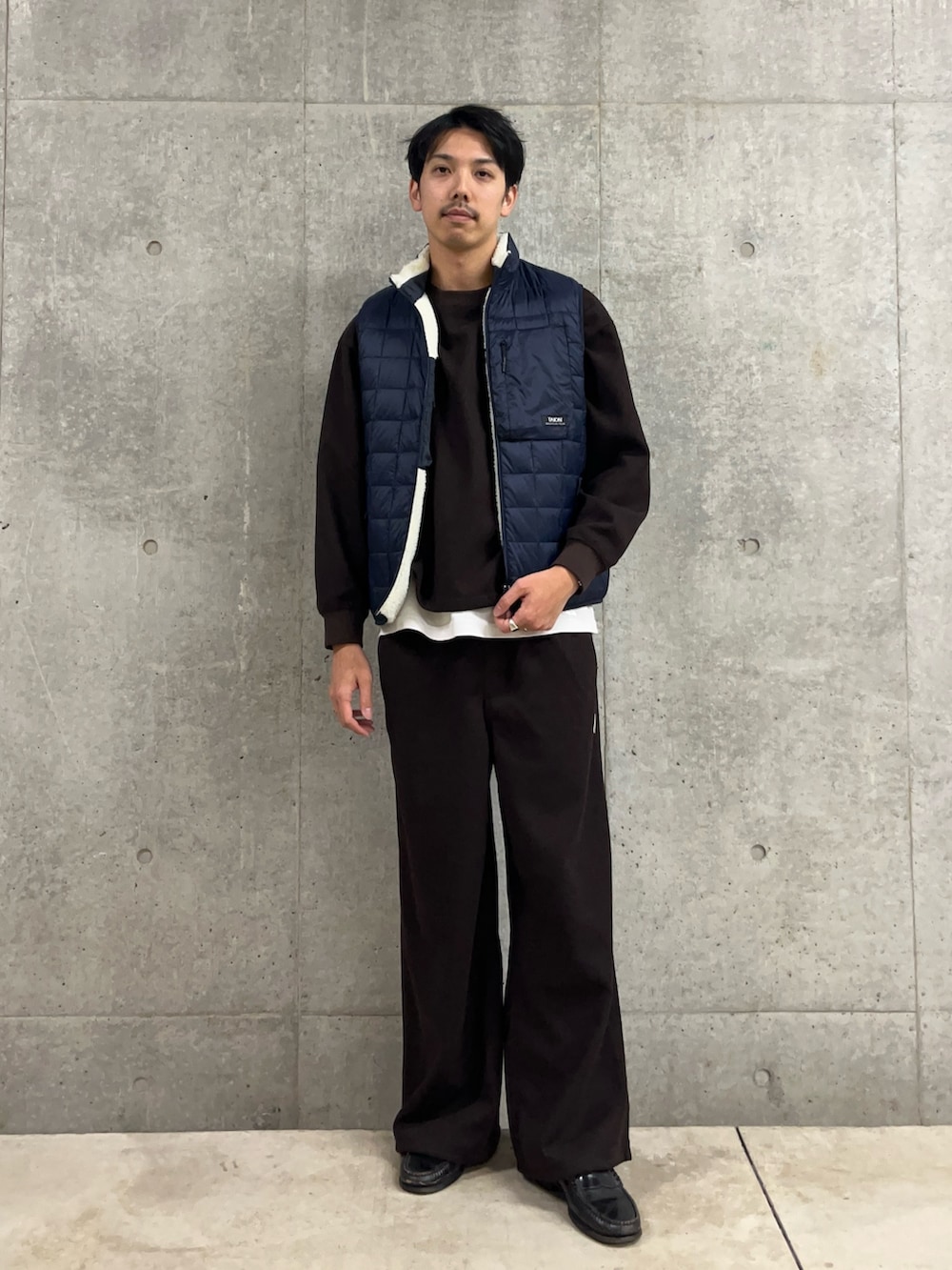 ブラウン系のスウェット、ホワイト系のダウンベスト、ブラウン系のその他パンツを着用したメンズの冬コーディネートの2枚目の写真