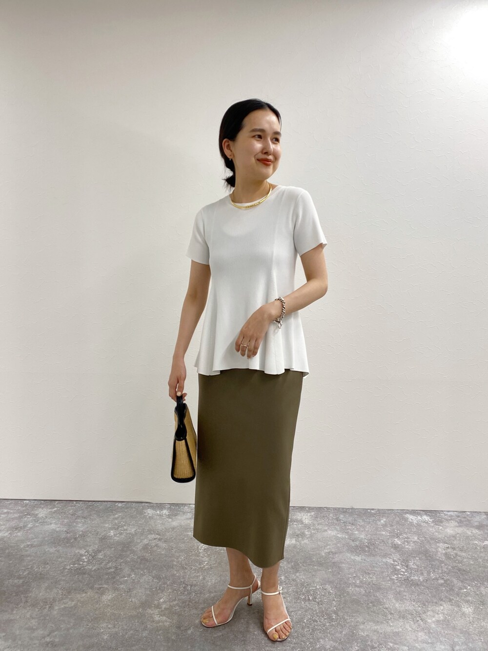 ホワイト系のニット/セーター、グレー系のスカート、ブラック系のトートバッグを着用したレディースの春コーディネートの2枚目の写真