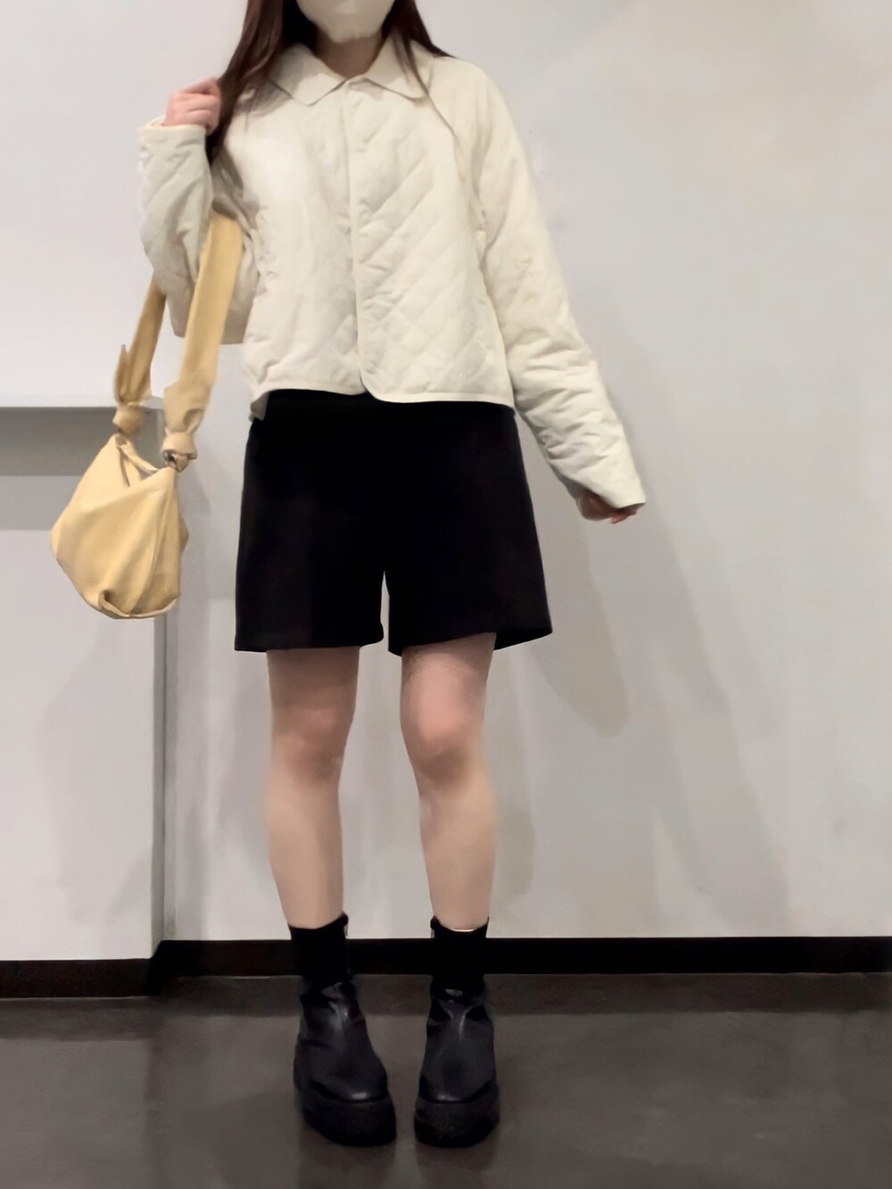 イエロー系のトートバッグ、ブラック系のブーツ、ホワイト系のダウンジャケット/コートを着用したレディースの冬コーディネートの2枚目の写真