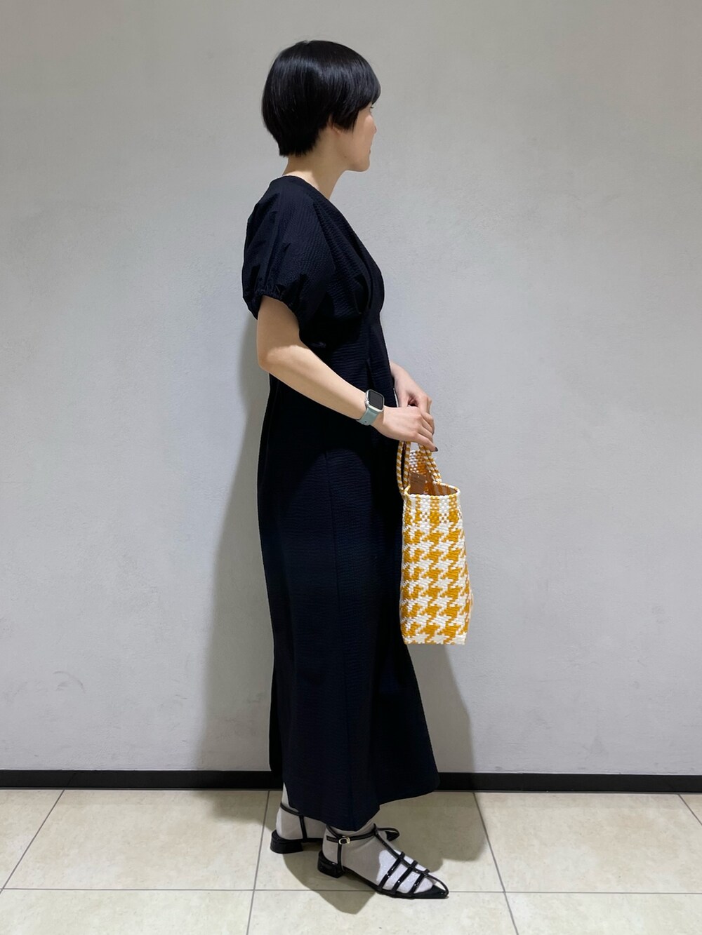 ブラック系のワンピース、イエロー系のトートバッグ、ブラック系のサンダルを着用したレディースの春コーディネートの2枚目の写真