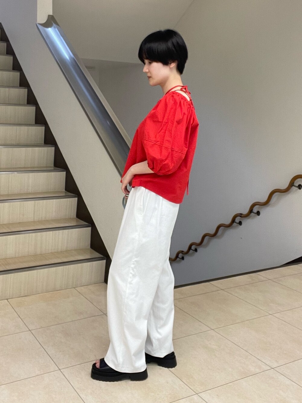 レッド系のシャツ/ブラウス、ホワイト系のスラックス、ブラック系のサンダルを着用したレディースの春コーディネートの2枚目の写真