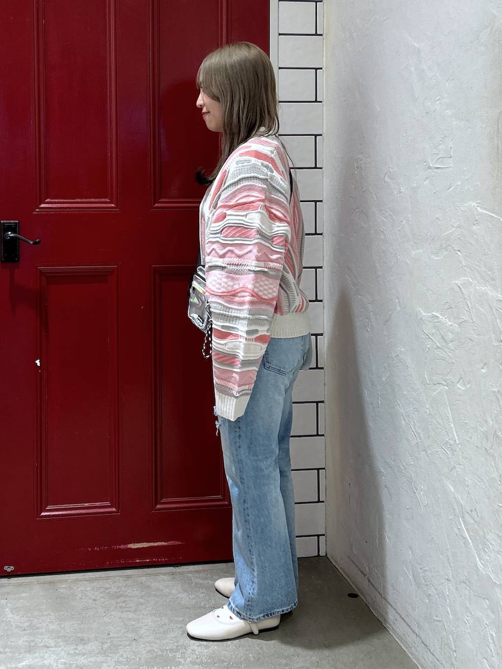 グレー系のショルダーバッグ、ホワイト系のパンプス、ブルー系のデニムパンツを着用したレディースの冬コーディネートの2枚目の写真