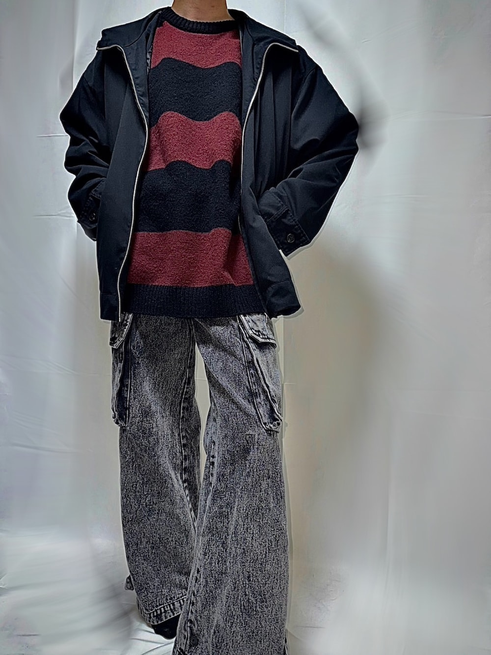 レッド系のニット/セーター、ブラック系のマウンテンパーカー、ブラック系のカーゴパンツを着用したメンズの秋コーディネートの2枚目の写真