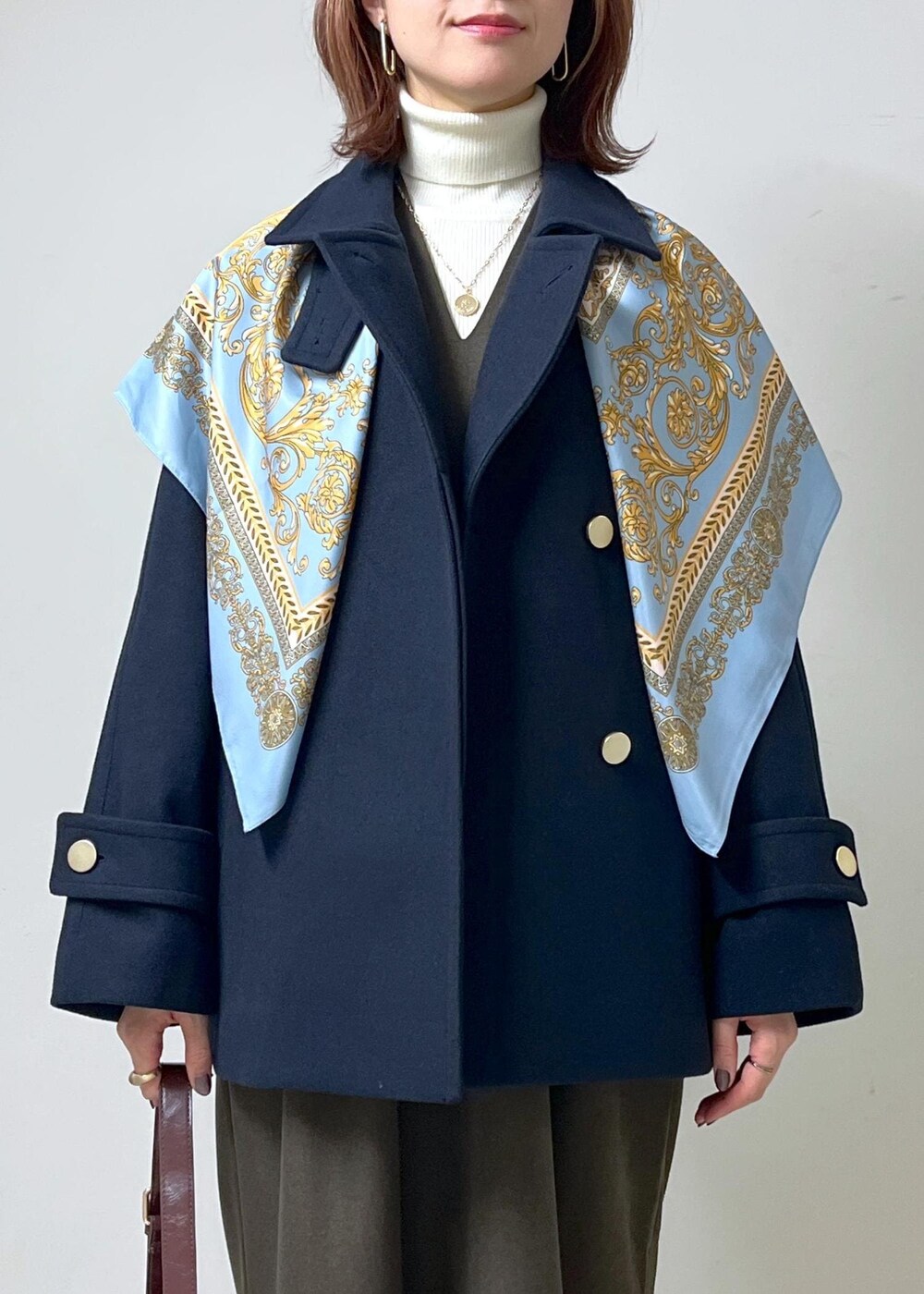 レッド系のショルダーバッグ、ホワイト系のニット/セーター、ブラウン系のブーツを着用したレディースの秋コーディネートの2枚目の写真