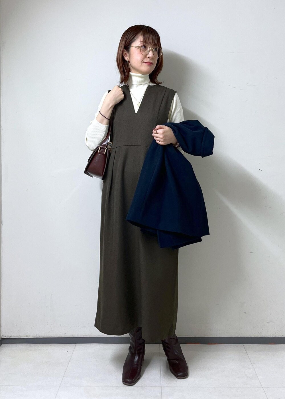 レッド系のショルダーバッグ、ホワイト系のニット/セーター、ブラウン系のブーツを着用したレディースの秋コーディネートの6枚目の写真